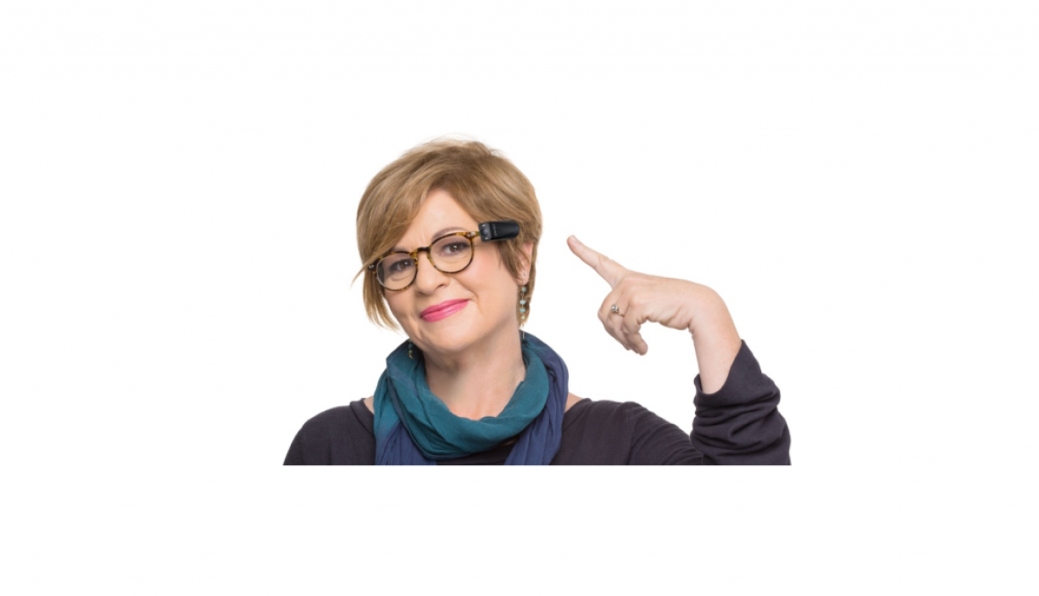 Woman wearing glasses with MyEye Pro attached, pointing to the device with a smile.