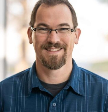 Nick May Nick May with glasses and a beard wearing a blue checkered shirt, representing the Vision Matters team and mission.