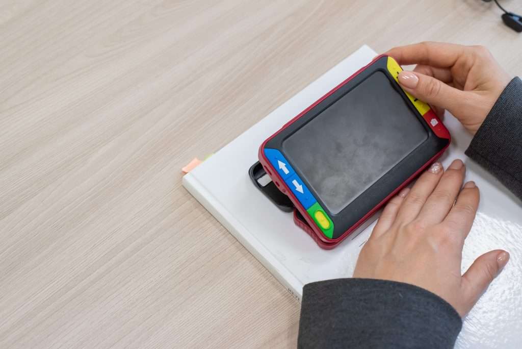 A person using handheld electronic magnifiers on a book to assist with reading and improving visual accessibility.